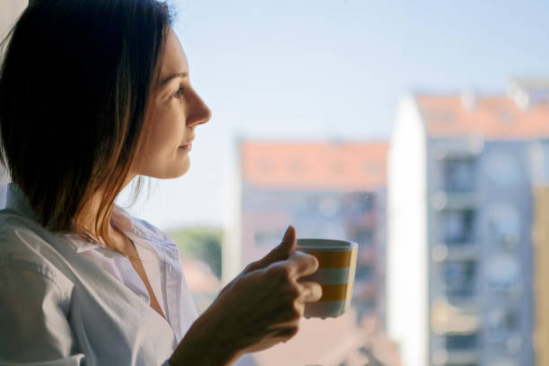 istock Young Women waking up ,drinking coffee looking through window 1211116423