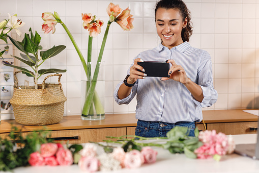 Young smiling woman using a smartphone to take a pictures of flowers