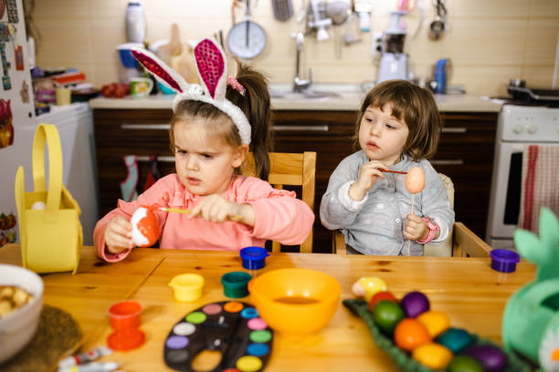 istock Curious little girl looking at her sister how she paint easter egg so she could do the same 1211125222