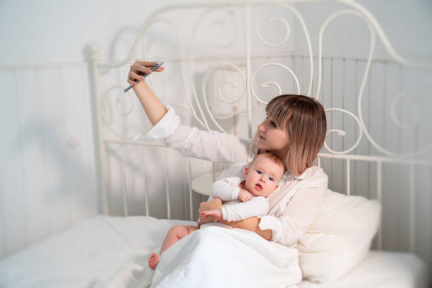 istock mom with baby in bed taking selfies 1211128188