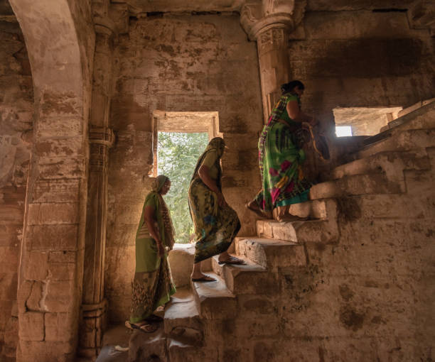 Three women walk up stairs inside an ancient fort Junagadh, Gujarat, India - December 2018: Three Indian women walk up an old staircase inside the dark interiors of the ancient Uparkot Fort. junagadh stock pictures, royalty-free photos & images