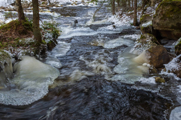 Stream in a forest with whirling water and ice in beautiful shapes on both sides, picture from Mellansel Vasternorrland, Sweden.