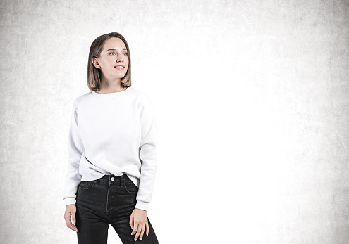 Portrait of inspired young and beautiful woman with short hair in casual clothes standing near concrete wall. Concept of education and youth. Mock up