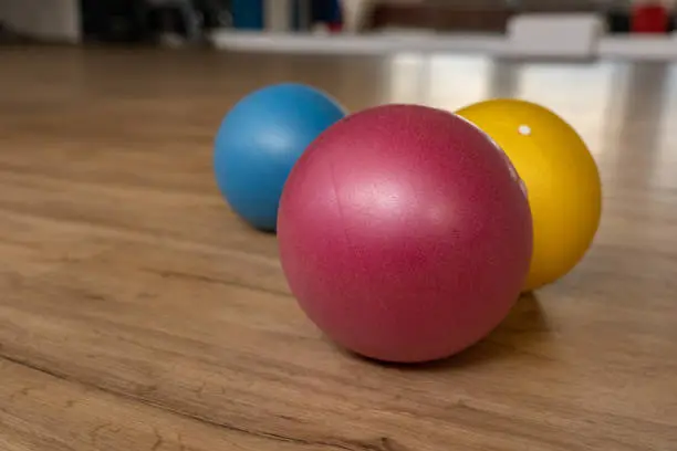 Photo of Three small and colorful gymnastic balls on wooden floor of a gymnastic hall of a group fitness center.