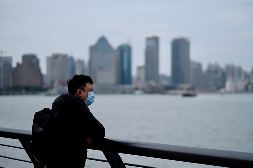 Shanghai/China-March.2020: Coronavirus 2019-nCoV pneumonia in Wuhan has been spreading into many cities. One man wearing surgical mask leaning on balustrade at the bund in China