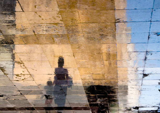 silhuetas de sombra de reflexo embaçado de uma mulher e uma criança andando em uma rua molhada em um dia ensolarado de verão - wet dress rain clothing - fotografias e filmes do acervo