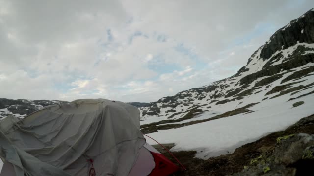 A young couple putting up the tent in the nearby of Trolltunga, Norway. Wild camping in the nature. Couple is having fun. They are surrounded by snow. Winter mountain climbing. Freedom and adventure.