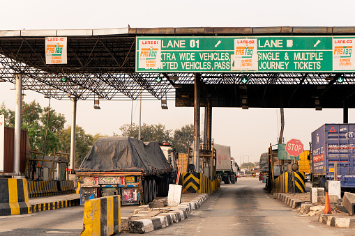 Delhi, India - circa 2020 : Empty toll booth on indian highway with FASTag callout on the headboard and traffic waiting. This mandatory RFID tag makes cashless digital payment necessary on Indian roads
