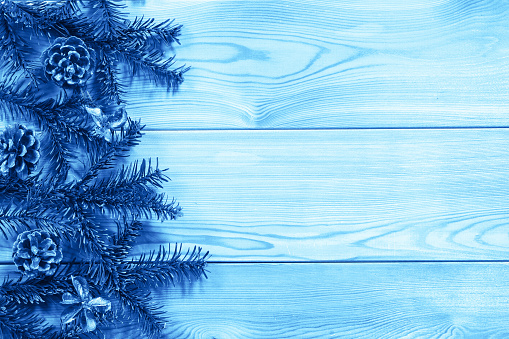 Green fir branches with pine cones on the edge of a textured wooden table. Tinting in Classic Blue, Space for text