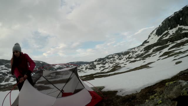 A young couple putting up the tent in the nearby of Trolltunga, Norway. Wild camping in the nature. Couple is having fun. They are surrounded by snow. Winter mountain climbing. Freedom and adventure.