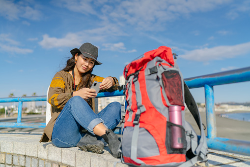 A young female solo traveler is using a smart phone while resting.