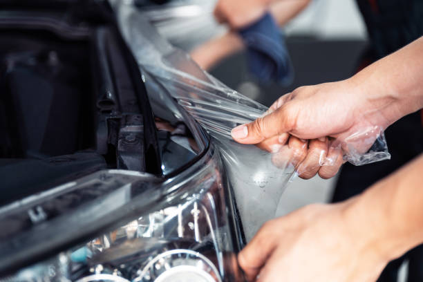 istock PPF installation process, close-up stretching removing an old transparent film on a car headlight and hood by hand. Automobile professional service. 1211166341