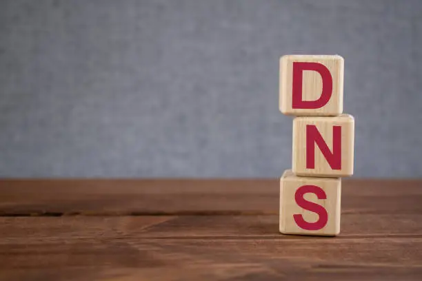 DNS - (Domain Name System) acronym on wooden cubes on dark wooden backround. Business concept.