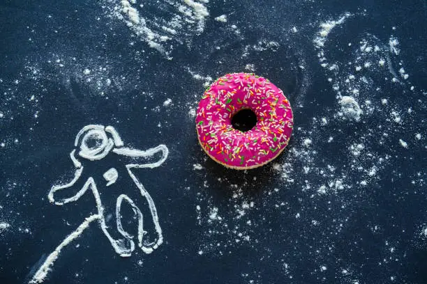 Photo of top view flat lay creative still life with pink donut and spaceman made from flour on a black background