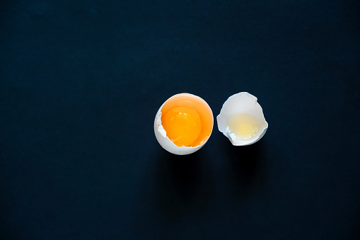 top view of a broken egg shell with a yolk on a black background, copy space
