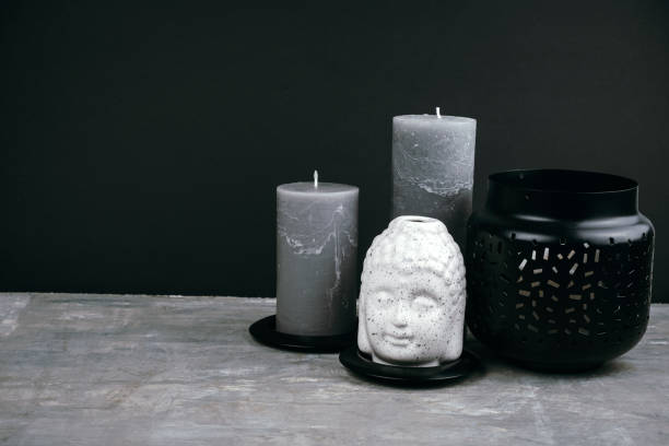 gray candles and white  ceramic Buddha head on a table opposite black wall