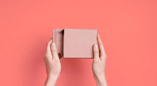istock Female hands open empty cardboard box on pink background. Top view 1211174286