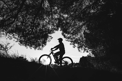 Cyclist silhouette at sunset, with lens flare effect. Biking sport concept. Monochorme version.