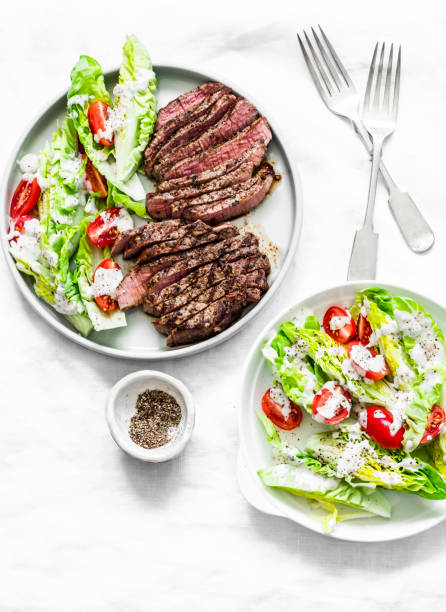 istock Beef medium rare steak and lettuce cherry tomatoes yogurt dressing salad on a light background, top view 1211183982