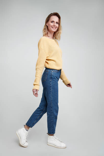 スリムで美しい。カジュアルウェアで魅力的な若い女性のフルレングススタジオショット空気に手を維持し、灰色の背景に対して歩いて笑顔 - women studio shot jeans young adult ストックフォトと画像