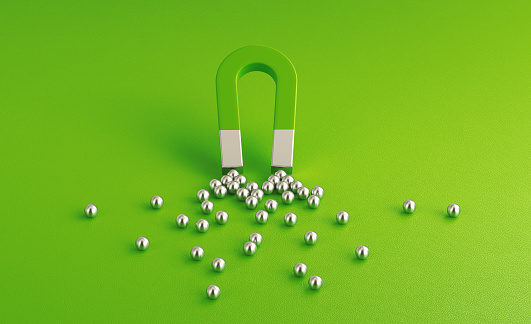 Silver spheres gravitated towards a green magnet on green background. Horizontal composition with copy space. Digital marketing concept.