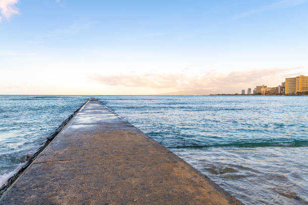 A beautiful stone pier walkway at the ocean at Waikiki Beach in Honolulu, HI, at sunset.