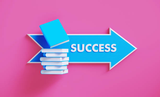 istock Book Stack Sitting over A Blue Arrow Shaped Directional Sign on Pink Background 1211192787