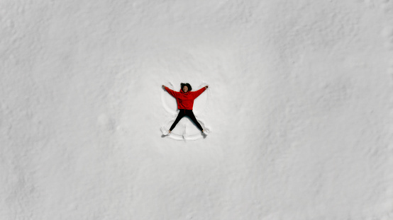 Aerial view of young woman having fun making snow angel.