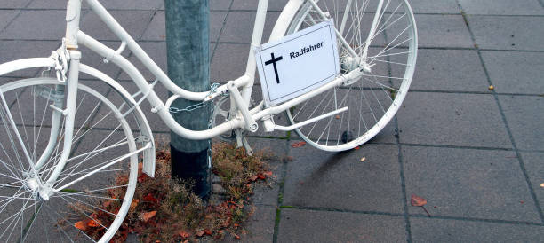 vista panorámica y primer plano de un monumento conmemorativo de la bicicleta fantasma funerario con un signo alemán - radfahrer - cruz para un ciclista asesinado. calle de la ciudad alemana en un día lluvioso. memorial a un ciclista que murió en accid - memorial roadside cross cross shape fotografías e imágenes de stock