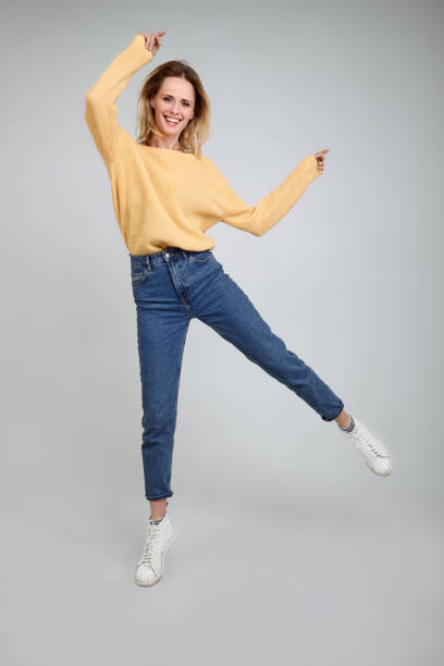 istock Active optimistic girl photographed at studio, jumps in air over white background, has broad smile, dressed in fashionable clothes. Motion is my life 1211193653