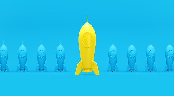 Yellow and blue rockets sitting in a row over turquoise background. Horizontal composition with copy space. Standing out from the crowd and  new business concept.