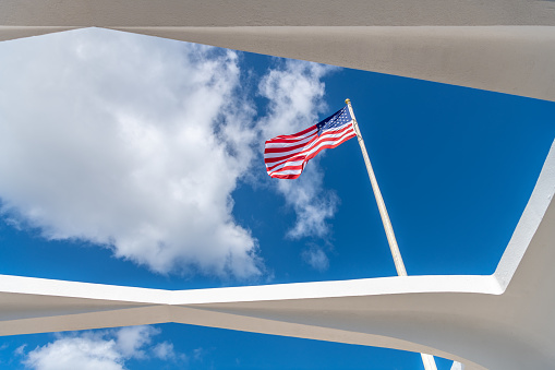 Honolulu, HI / USA - January 27, 2020: The U.S. flag flies above the beautiful USS Arizona Memorial Monument at Pearl Harbor. The memorial opened in 1962 and was designed by Alfred Preis.