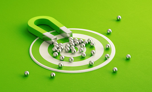 Silver spheres gravitated towards a green magnet on green target background. Horizontal composition with copy space. Digital marketing concept.