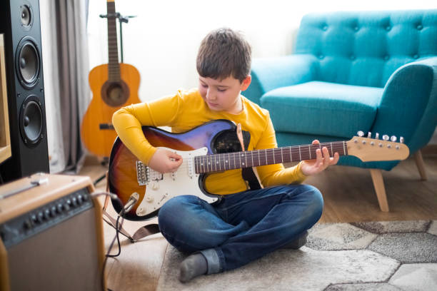 istock Little boy playing electric guitar at home 1211200118