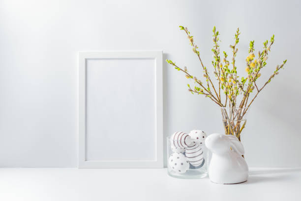 istock Home interior with easter decor. Mockup with a white frame and willow branches in a vase on a light background 1211201481