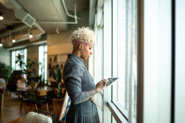 Tattooed businesswoman using digital tablet close to the window Tattooed businesswoman using digital tablet close to the window leanincollection stock pictures, royalty-free photos & images