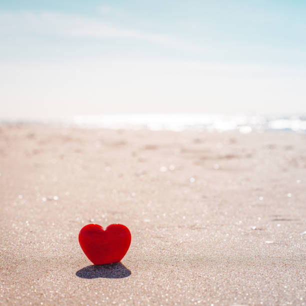 istock Romantic symbol of red heart on the sand beach 1211207526