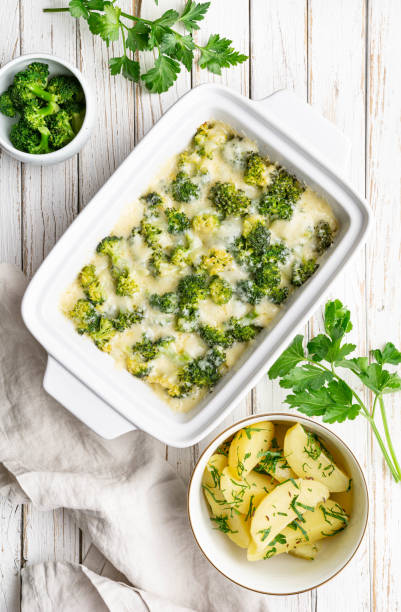 Broccoli and cheese casserole served with boiled potatoes on white wooden background stock photo