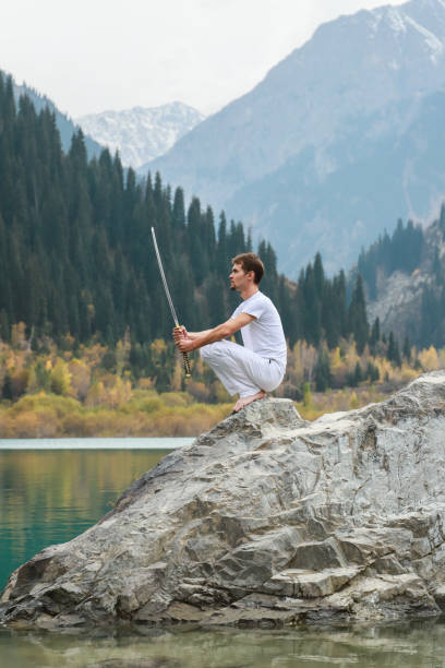 istock A wise man sits on a stone and holds a sword in his hands. Mountain Lake background 1211214939