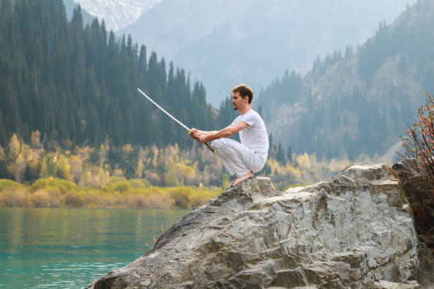 istock A wise man sits on a stone and holds a sword in his hands. Mountain Lake background 1211215989