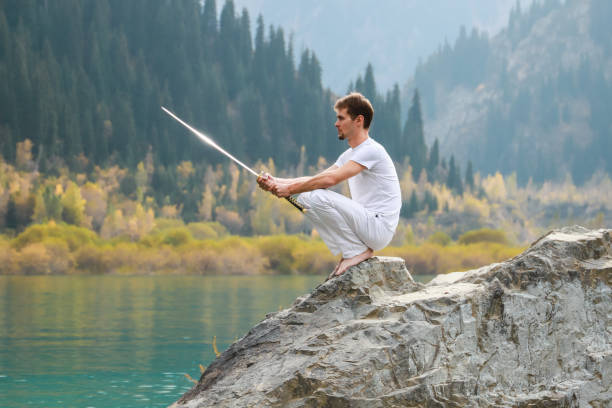 istock A wise man sits on a stone and holds a sword in his hands. Mountain Lake background 1211215997