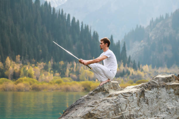 istock A wise man sits on a stone and holds a sword in his hands. Mountain Lake background 1211216044