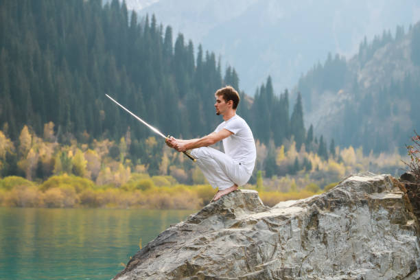 istock A wise man sits on a stone and holds a sword in his hands. Mountain Lake background 1211216062