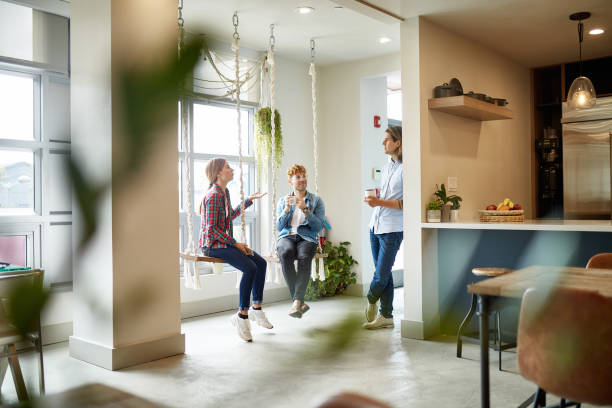 Casual Businesspeople Talking on Break in Coworking Office Personal perspective of male and female freelancers in 20s and 30s relaxing on swings and talking during coffee break in coworking office environment. personal perspective standing stock pictures, royalty-free photos & images