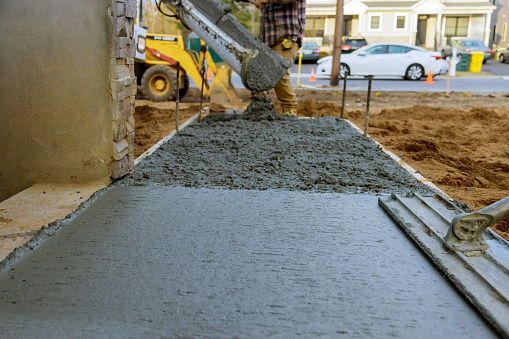 Construction worker pouring reinforced concrete cement for sidewalk in new residential home