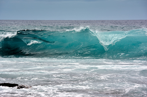 Looking at illuminated breaking wave in vibrant blue color turning in turquoise shades hitting close to shore
