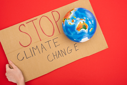 Cropped view of woman holding placard with stop climate change lettering and globe on red, global warming concept