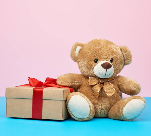 istock cute little brown teddy bear holds a brown box with a red ribbon 1211218927