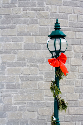 green lampost against a white brick wall wrapped in garland with a little snow on it