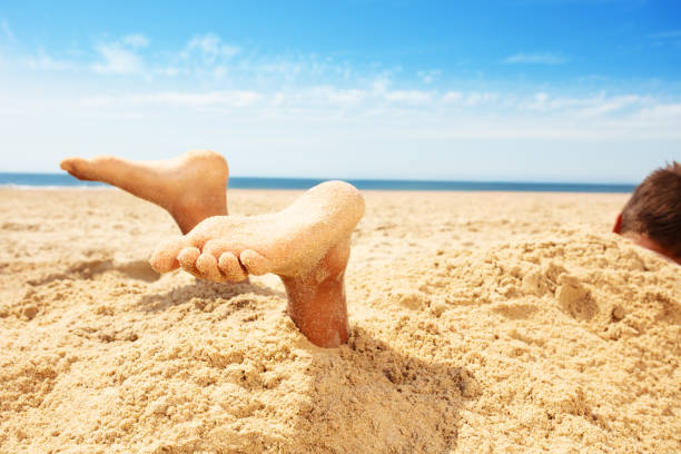 ноги и ноги мальчика, покрытого песком в игре на море - lifestyles child beach digging стоковые фото и изображения